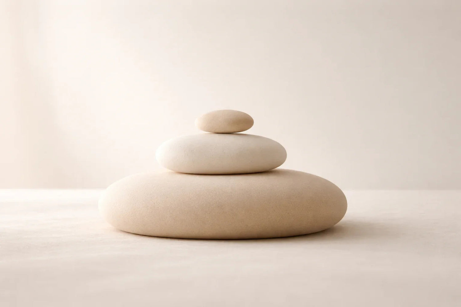 Trois galets empilés en équilibre sur une surface beige sable, dans une ambiance minimaliste et apaisante aux tons neutres.